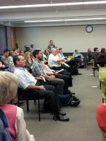 Audience members sitting in rows of chairs in an indoor office conference room