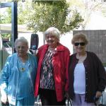 three elderly women standing in the shade with trees behind them